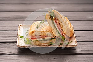 Grilled and pressed bread with smoked ham, cheese, tomato and lettuce served on plate.