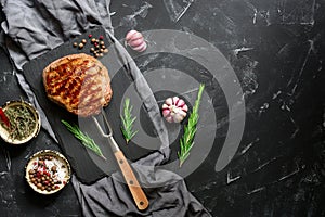 Grilled ribeye beef steak on the fork, black stone background. Top view, flat lay, copy space