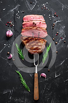 Grilled ribeye beef steak medium rare with spices and herbs on a black stone background. Top view, flat lay, copy space