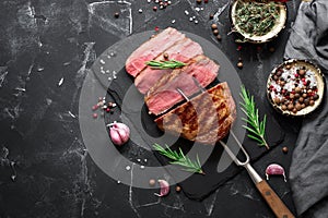 Grilled ribeye beef steak medium rare with spices and herbs on a black stone background. Top view, flat lay, copy space