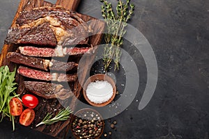 Grilled ribeye beef steak with red wine, herbs and spices on a dark stone background. Top view with copy space for your text