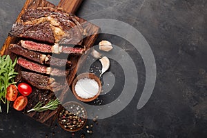 Grilled ribeye beef steak with red wine, herbs and spices on a dark stone background. Top view with copy space for your text