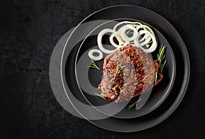 Grilled ribeye beef steak with rosemary and marinated onion on a black stone table