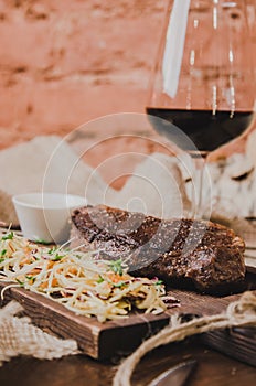 Grilled ribeye beef steak with stew cabbage and wineglass of red wine, herbs and spices over brown sackcloth on wooden