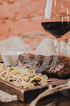 Grilled ribeye beef steak with stew cabbage and wineglass of red wine, herbs and spices over brown sackcloth on wooden