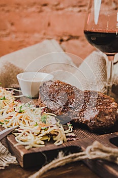 Grilled ribeye beef steak with stew cabbage and wineglass of red wine, herbs and spices over brown sackcloth on wooden