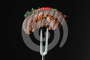 Grilled ribeye beef steak with thyme and chili pepper on a black background. copy space for text