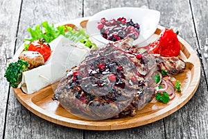 Grilled Ribeye Steak on bone with berry sauce, fresh salad and grilled vegetables on cutting board on wooden background