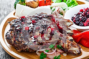 Grilled Ribeye Steak on bone with berry sauce, fresh salad and grilled vegetables on cutting board on wooden background