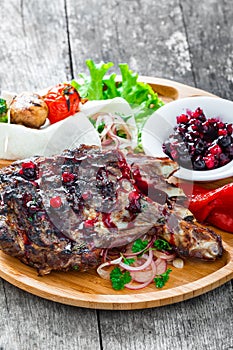 Grilled Ribeye Steak on bone with berry sauce, fresh salad and grilled vegetables on cutting board on wooden background