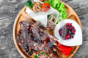 Grilled Ribeye Steak on bone with berry sauce, fresh salad and grilled vegetables on cutting board on wooden background