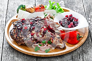 Grilled Ribeye Steak on bone with berry sauce, fresh salad and grilled vegetables on cutting board on wooden background