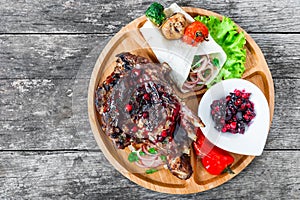 Grilled Ribeye Steak on bone with berry sauce, fresh salad and grilled vegetables on cutting board on wooden background