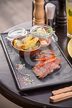 Grilled Ribeye Steak with potatoes and vegetable salad on stone board on the table at restaurant