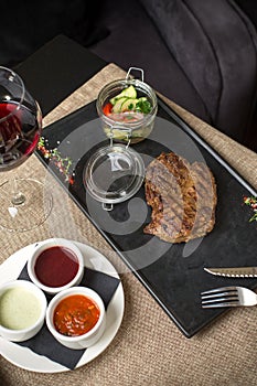 Grilled Ribeye Steak with vegetable salad on stone board and glass of red wine on the table at restaurant