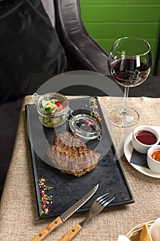 Grilled Ribeye Steak with vegetable salad on stone board and glass of red wine on the table at restaurant