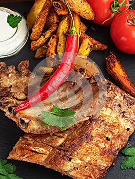 Grilled ribs with French fries and vegetables on the dark background. Shallow depth of field. Vertical orientation