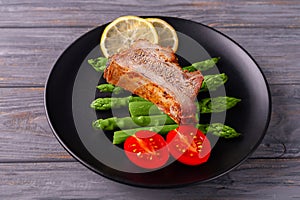 Grilled ribs with green asparagus, tomatoes and lemon on a plate