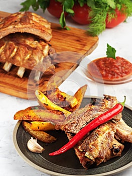 Grilled ribs with idaho potatoes and vegetables on the plate, on the grey background. Shallow depth of field. Vertical orientatio