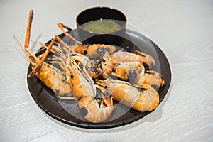 Grilled river shrimps with chili seafood sauce on black plate.