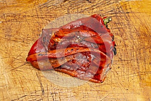 grilled roasted and peeled red peppers on a textured wooden   board