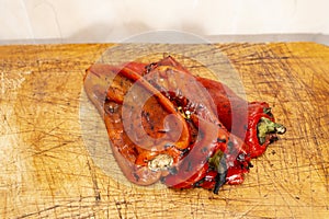 grilled roasted and peeled red peppers on a textured wooden chopping board, close up