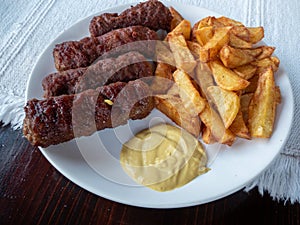 Grilled romanian traditional food meat rolls called mititei, mici - close-up with french fries and mustard