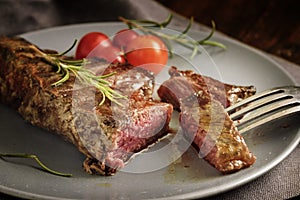 Grilled rump steak with rosemary garnish and tomatoes on a gray