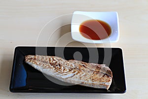 Grilled saba on black dish with dipping soy sauce and green spicy sauce