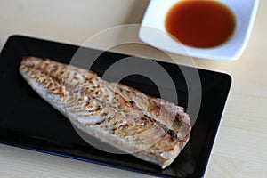 Grilled saba on black dish with dipping soy sauce and green spicy sauce