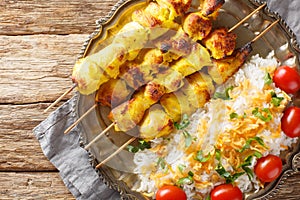 Grilled saffron chicken skewers with rice garnish close-up in a plate. horizontal top view