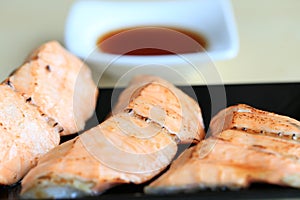 Grilled salmon on black dish with dipping soy sauce and green spicy sauce