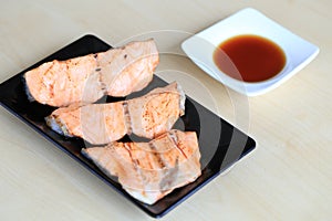 Grilled salmon on black dish with dipping soy sauce and green spicy sauce