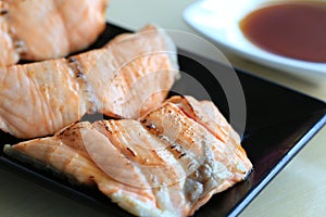 Grilled salmon on black dish with dipping soy sauce and green spicy sauce