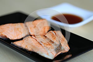 Grilled salmon on black dish with dipping soy sauce and green spicy sauce