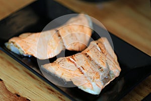 Grilled salmon on black dish with dipping soy sauce and green spicy sauce