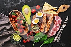 Grilled salmon with boiled egg, ham, vegetables and strawberries on a dark background. Keto diet dinner or lunch. Top view, flat