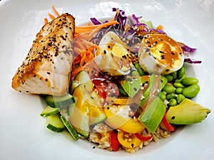 A grilled salmon with boiled eggs, avocado, lettuce, peas, tomatoes and carrots inside a white bowl
