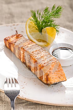 Grilled salmon fillet with lemon and soy sauce on white plate on tablecloth