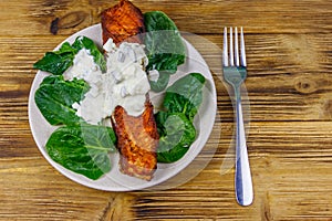 Grilled salmon fillet with spinach and tartare sauce on wooden table. Top view