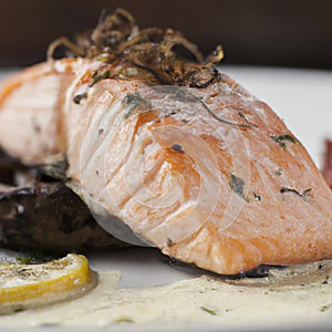 Grilled salmon fillet on a white plate with lemon or lime wedges, sauce and herbs. AI generated