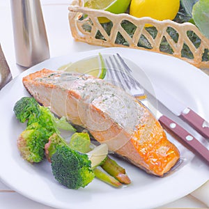 Grilled salmon fillet on a white plate with lemon or lime wedges, sauce and herbs. AI generated