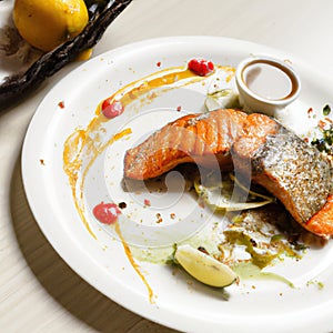 Grilled salmon fillet on a white plate with lemon or lime wedges, sauce and herbs. AI generated