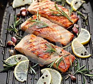 Grilled salmon fillets sprinkled with fresh herbs and lemon juice on a grill plate