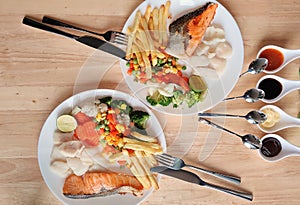 Grilled salmon fish and baked cod fish decorated with various vegetables corn carrot peas lemon french fries and sauces