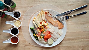 Grilled salmon fish and baked cod fish decorated with various vegetables corn carrot peas lemon french fries and sauces