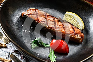 Grilled salmon fish steak with lemon slices and tomatoes in plate on wooden rustic background. Seafood, healthy food, close up