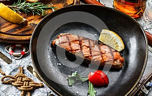 Grilled salmon fish steak with lemon slices and tomatoes in plate on wooden rustic background. Seafood, healthy food, close up