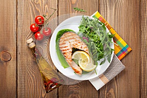 Grilled salmon, salad and condiments on wooden table