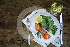 grilled salmon with spinach an wine on a dark rustic wooden table, view from above, copy space